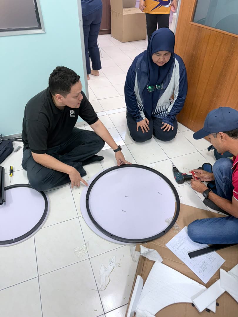 Three people on the floor assembling a round frame with a drill and the instruction sheet