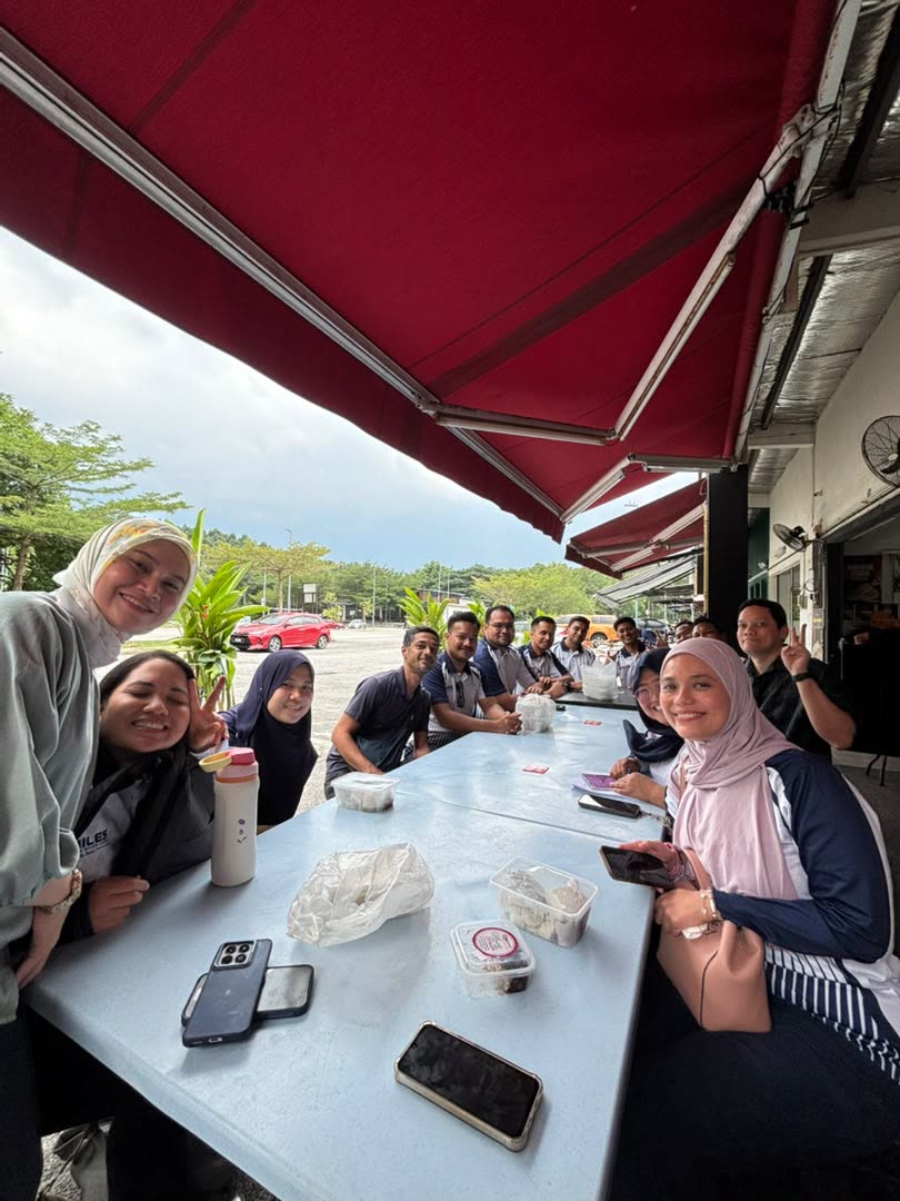 Committee members smiling around an outdoor table under a red awning